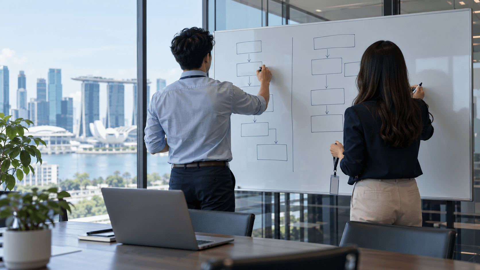 Two people seen from behind drawing a two-column diagram of boxes and arrows on a whiteboard in a glass meeting room